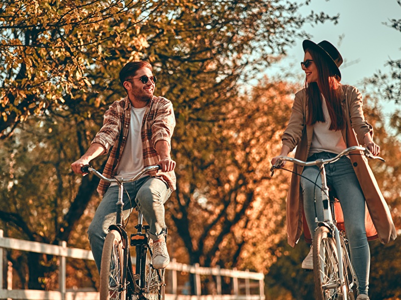 Man and woman cycling, laughing next to each other on a sunny autumn day.