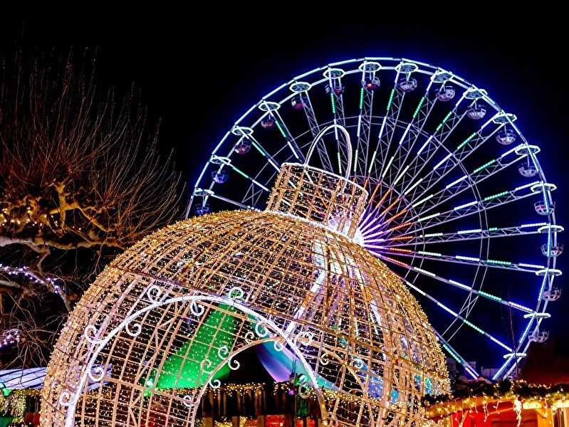 Illuminated Christmas decorations and a large Ferris wheel at night during a winter event, with colorful lights and a festive atmosphere