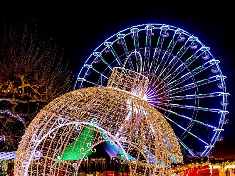 Illuminated Christmas decorations and a large Ferris wheel in the evening during a winter event, with colorful lights and a festive atmosphere