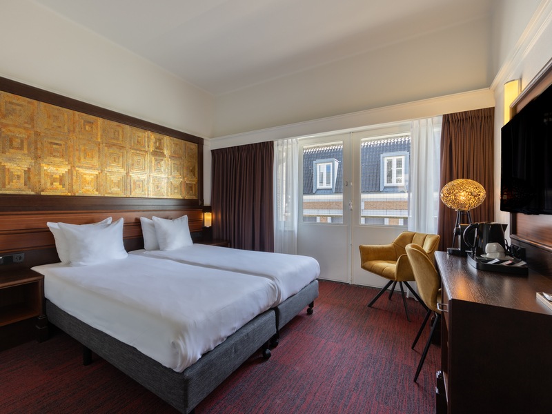 Deluxe room at Amrâth Hotel DuCasque with a dark bedspread and white duvet. In the corner, there is a chair with a side table.
